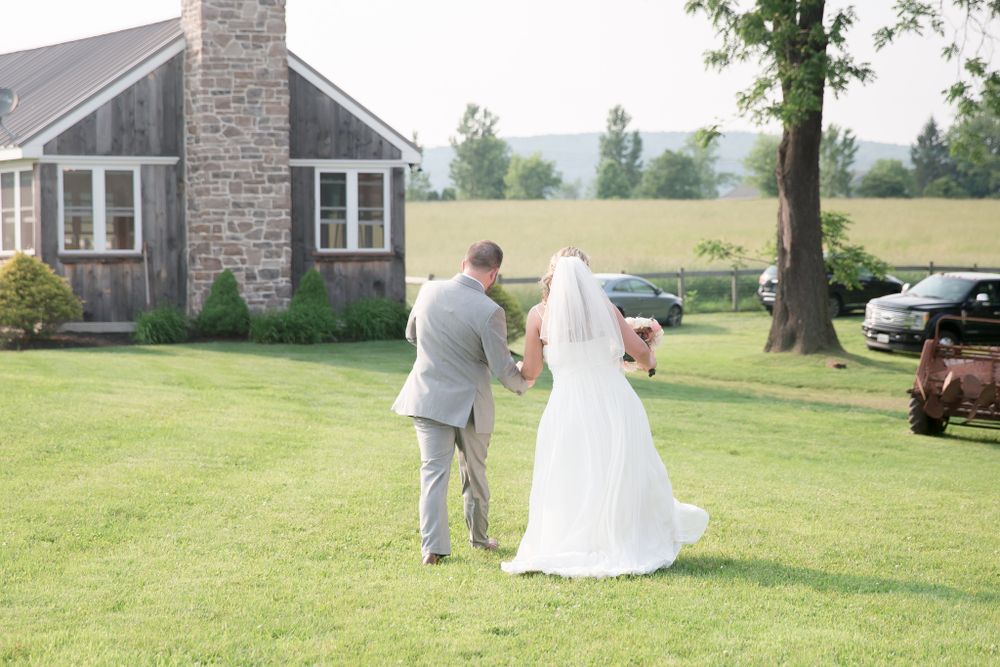 Couple walks towards stone cottage on grassy hillside after wedding ceremony.