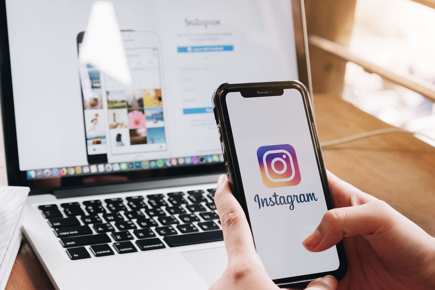 woman holding phone in front of laptop using Instagram