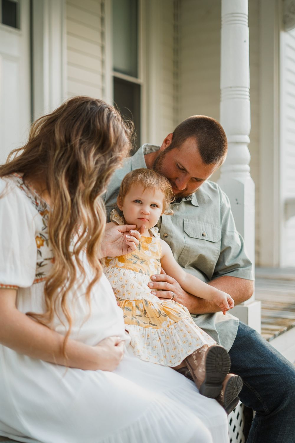 A family shares an intimate moment together on a white porch with columns.