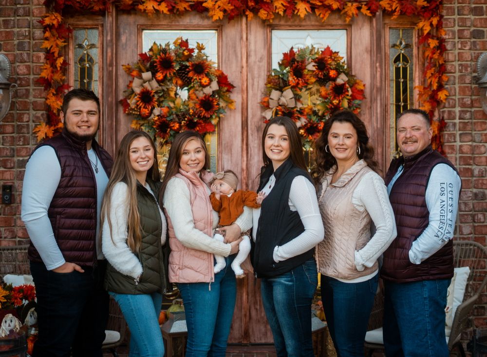Family group photo in front of doors decorated with fall wreaths and autumn decor.
