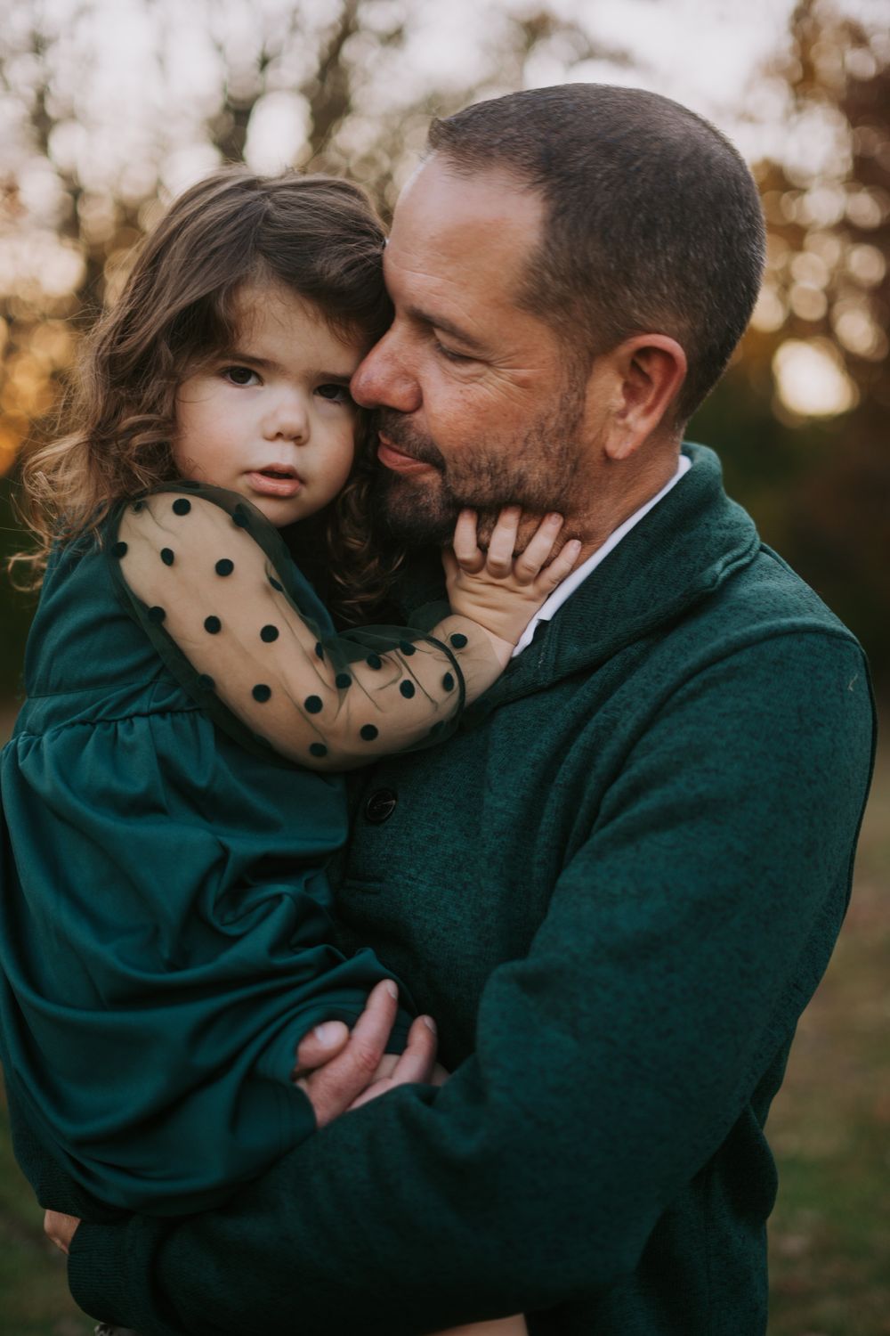 Tender moment between parent and child wearing green polka dot dress at sunset.