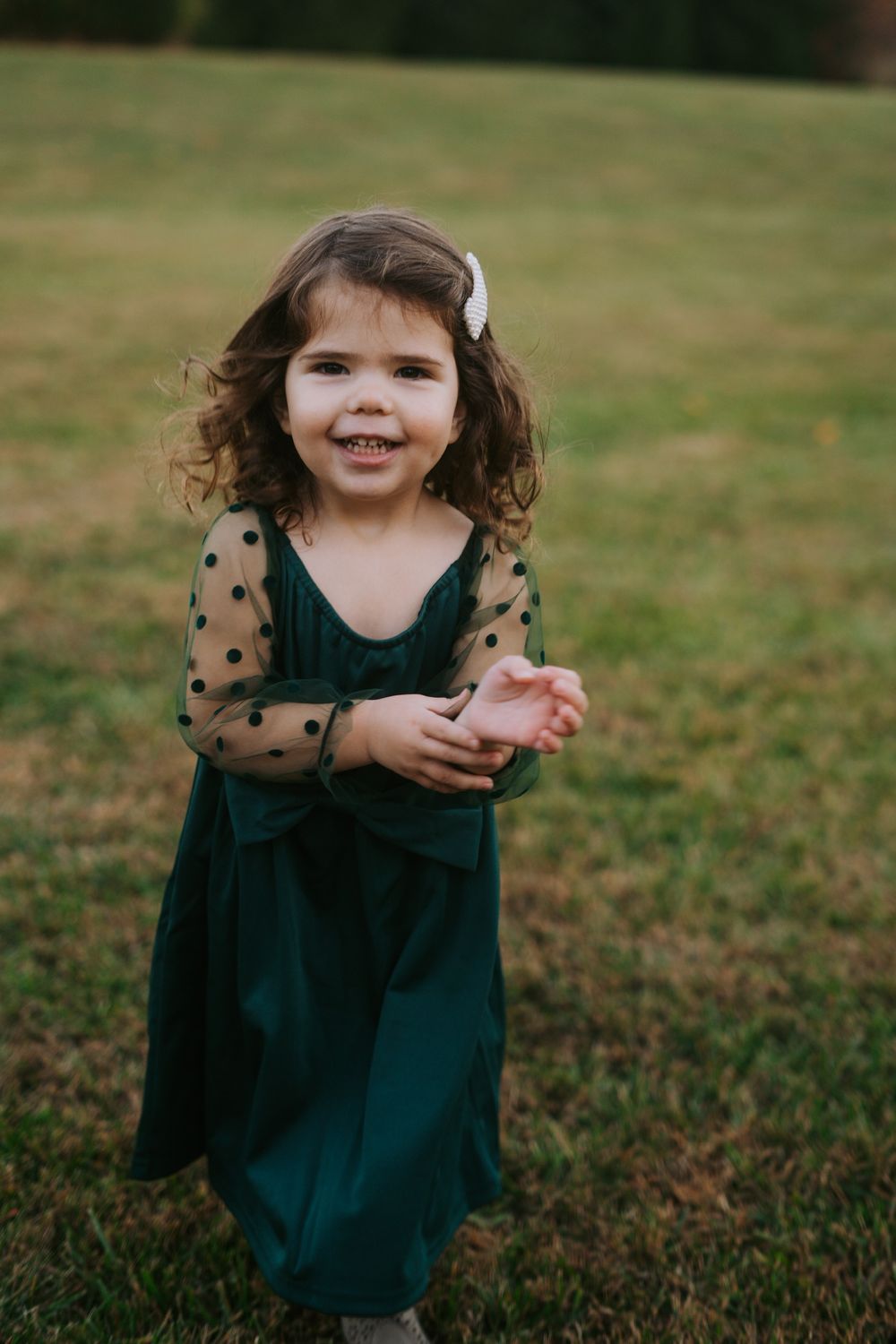 Young child in green dress with polka dot sleeves smiling outdoors.