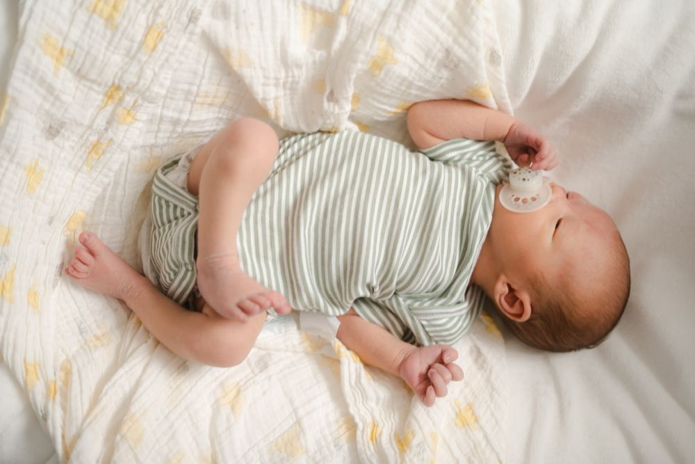 Baby in striped onesie lying on white patterned blanket.
