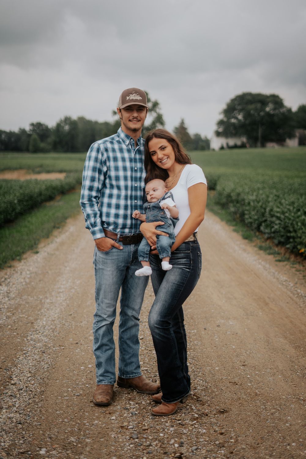 Family of three poses together on a rural dirt road with cloudy skies in the background.