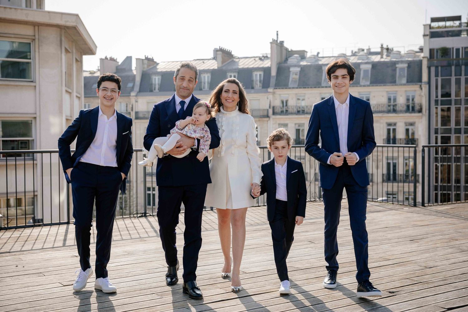 Family group walking together on a Parisian rooftop terrace with city buildings in background.