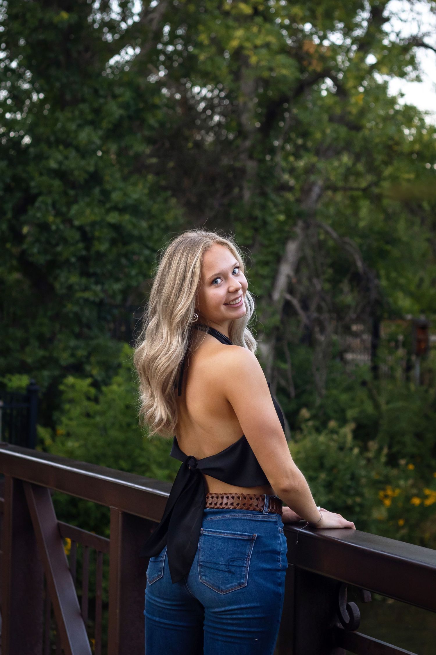 A candid outdoor portrait on a wooden deck surrounded by lush green trees.