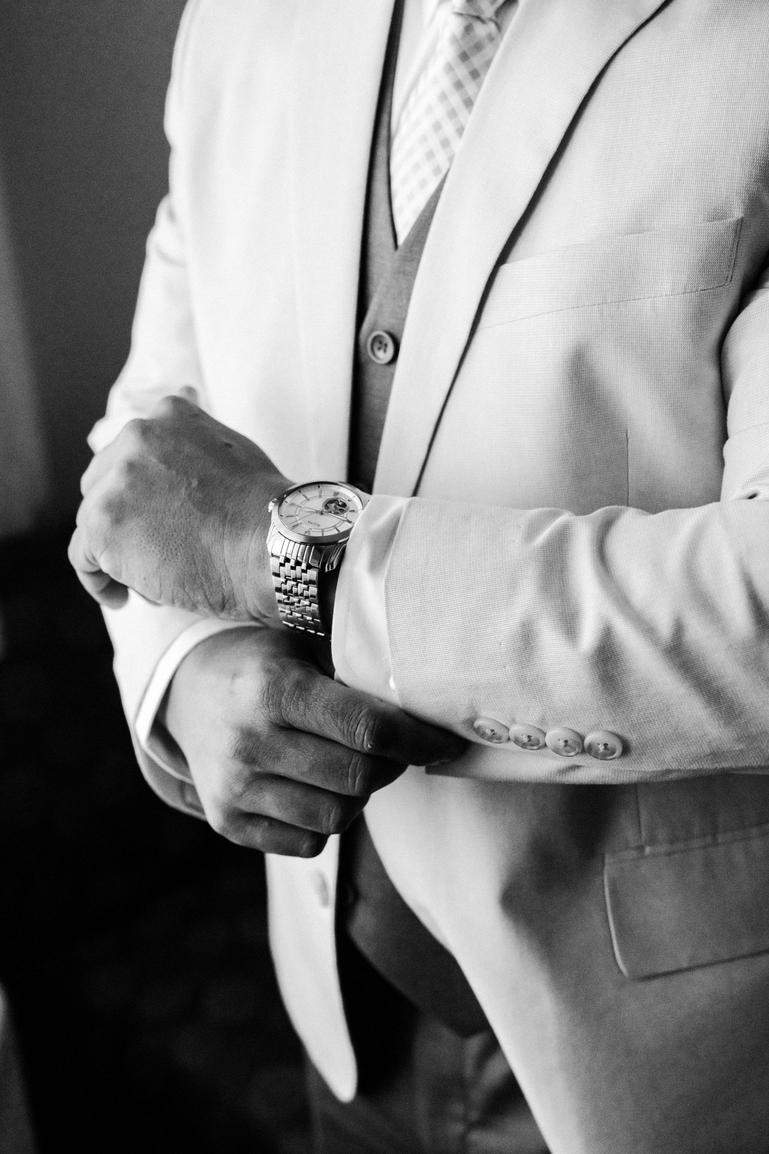 Close up of a person in white suit adjusting their silver watch.