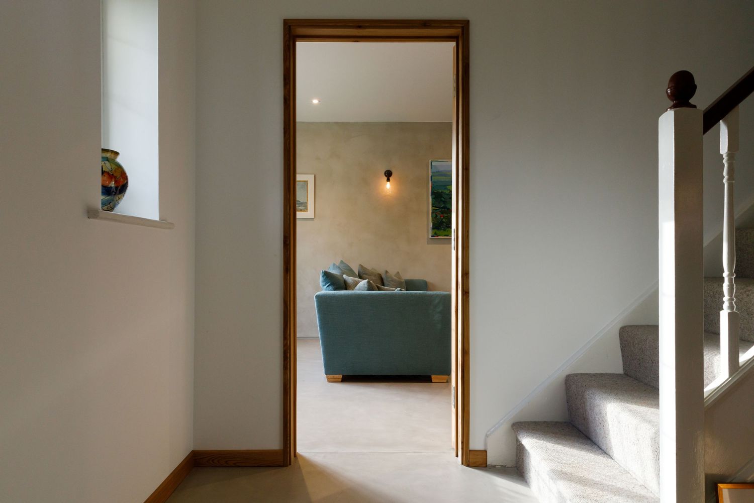 Modern hallway with white stairs and doorway leading to a teal sofa in an adjacent room taken during an interiors photoshoot.