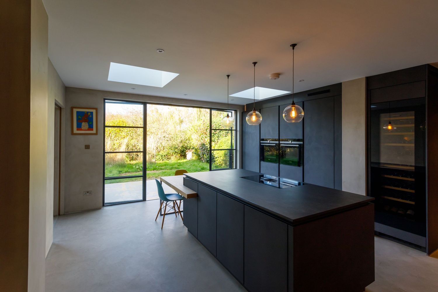 Modern kitchen with black island and pendant lights beneath skylight window overlooking garden taken during an interiors photoshoot