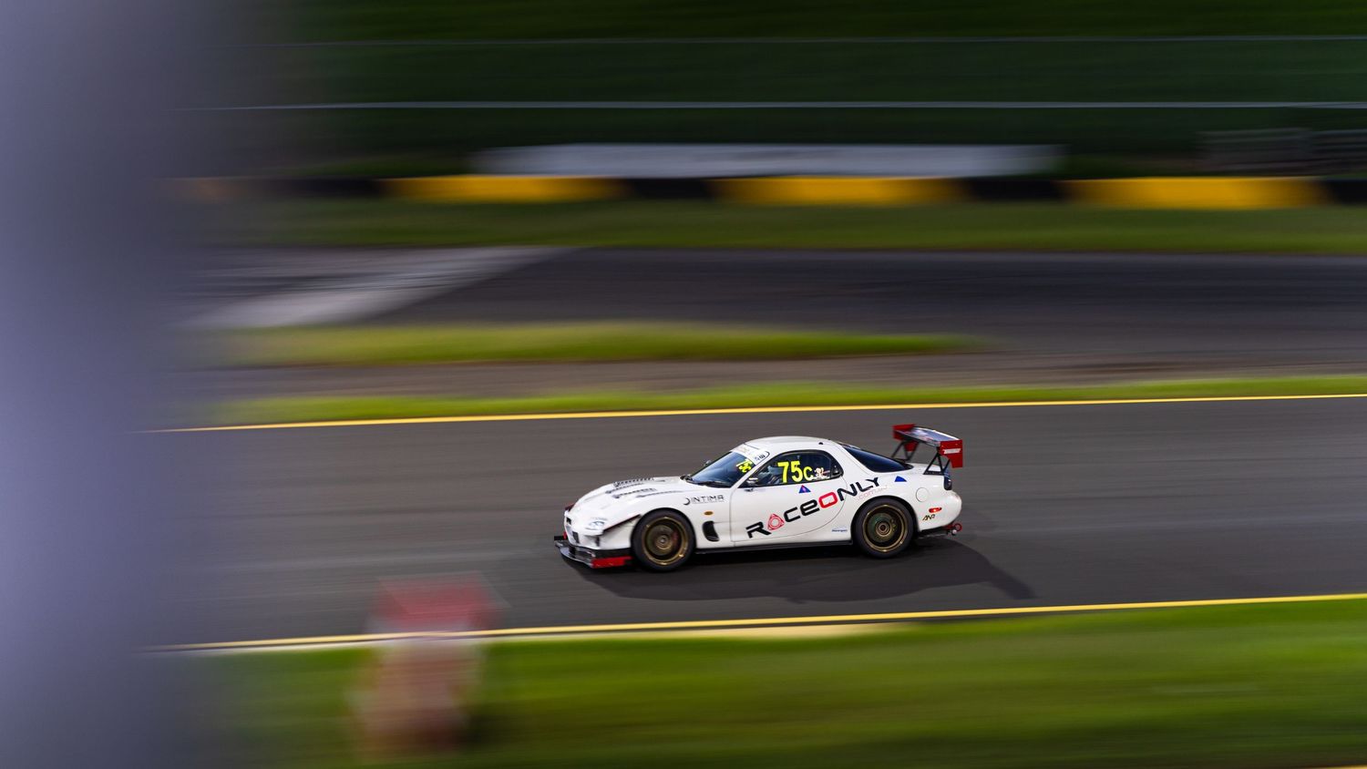 White race car photographed with motion blur effect on racing circuit.