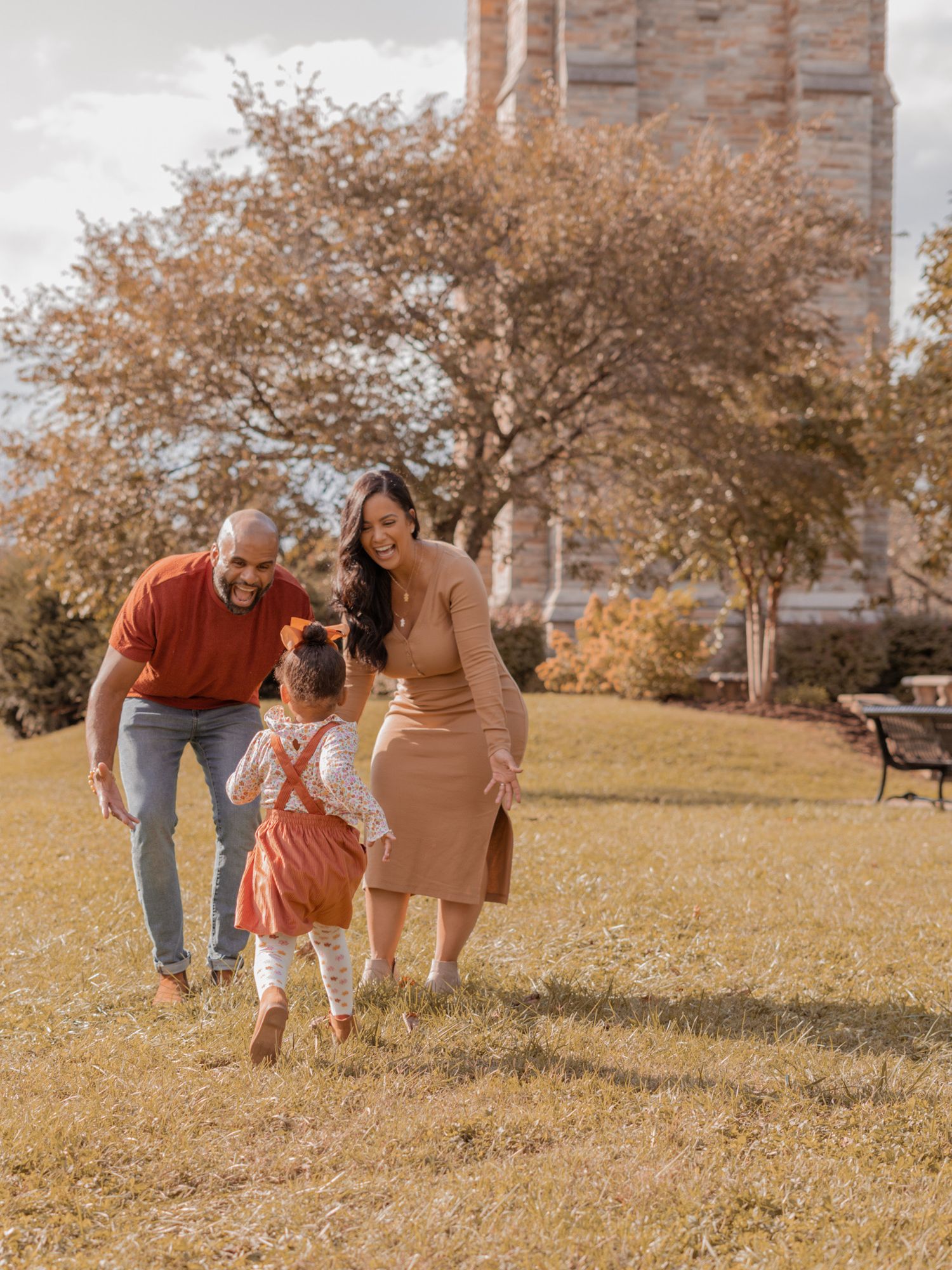 Family walking together on grass during golden hour near historic building.