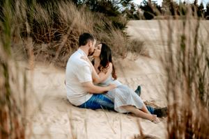 Couple embracing on sandy dunes surrounded by beach grass at golden hour.