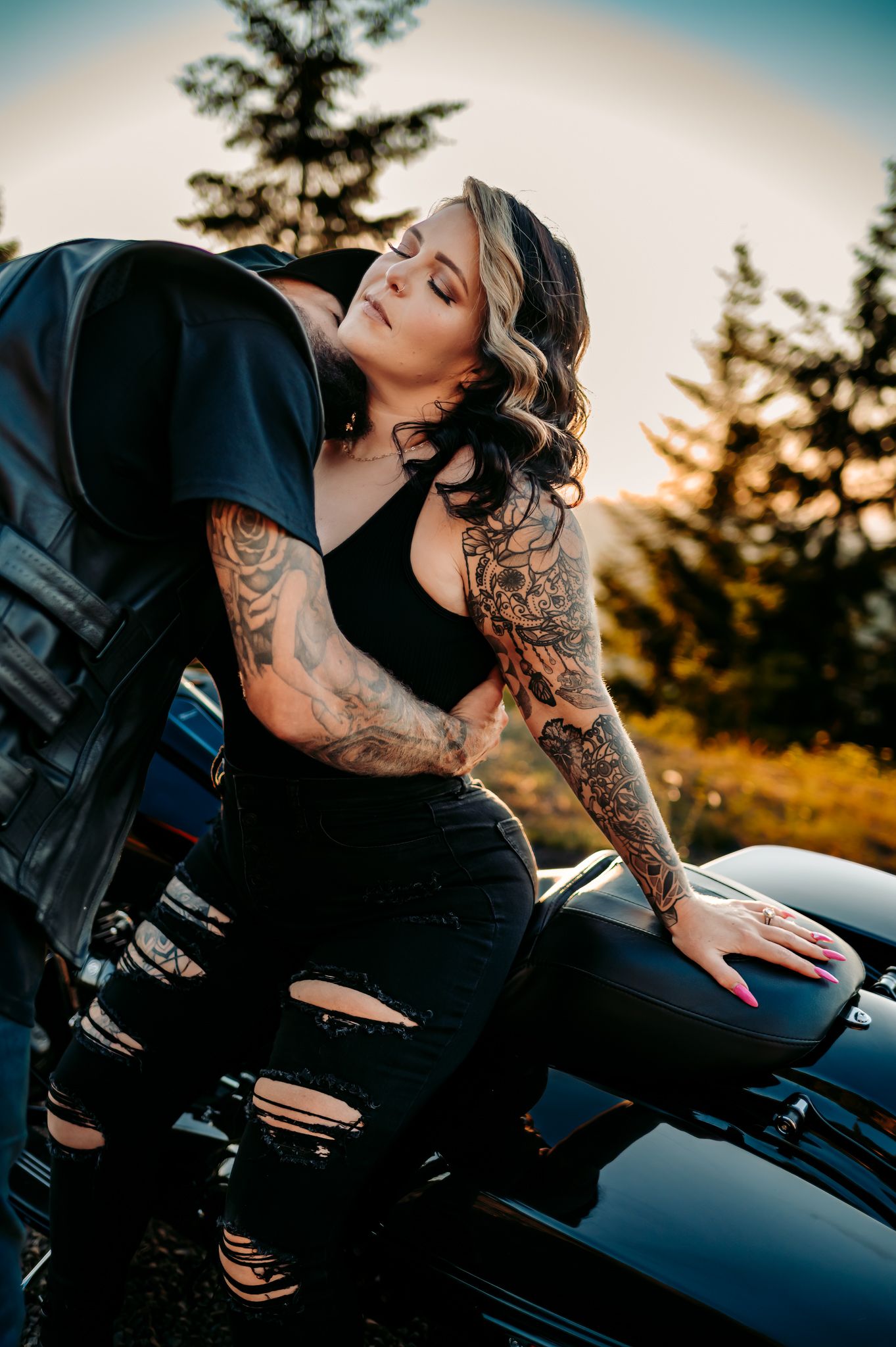 Tattooed couple embracing on a motorcycle during golden hour.