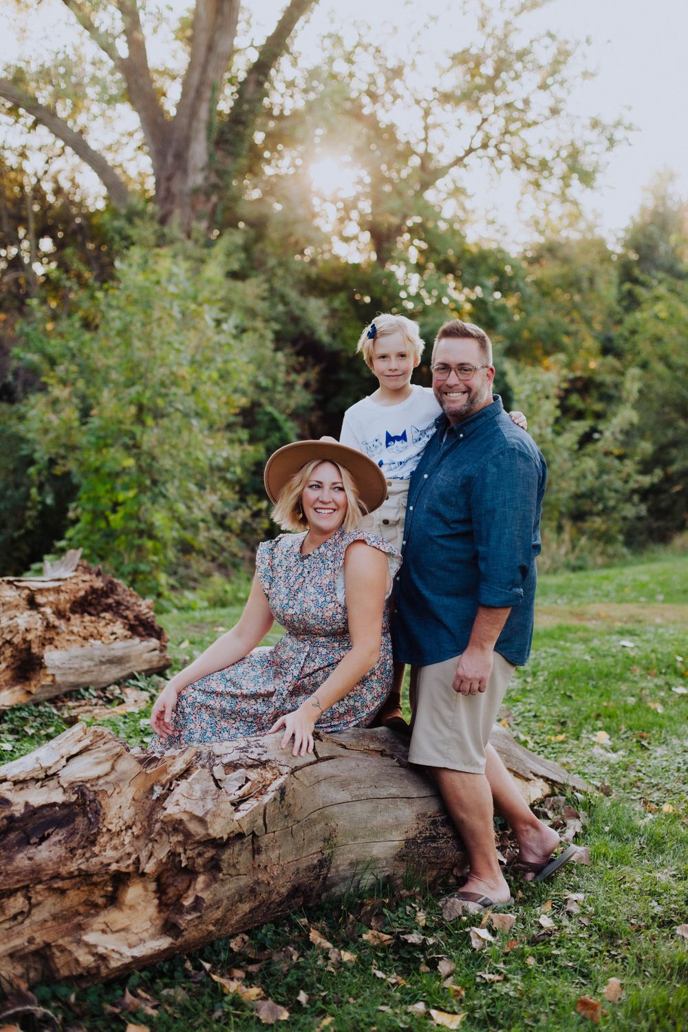 An intimate family portrait session on a weathered log with warm evening sunlight filtering through trees.