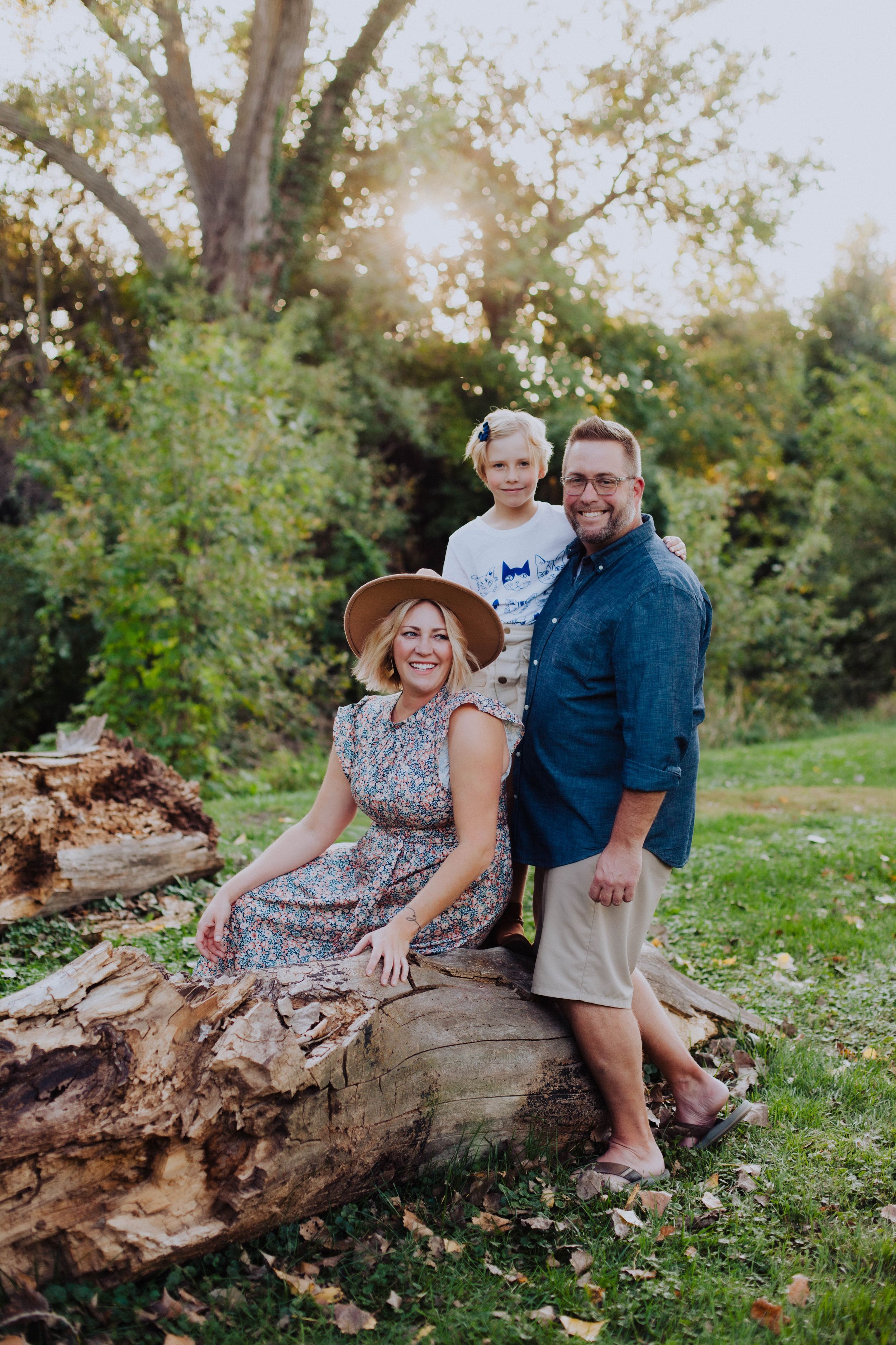 An intimate family portrait session on a weathered log with warm evening sunlight filtering through trees.
