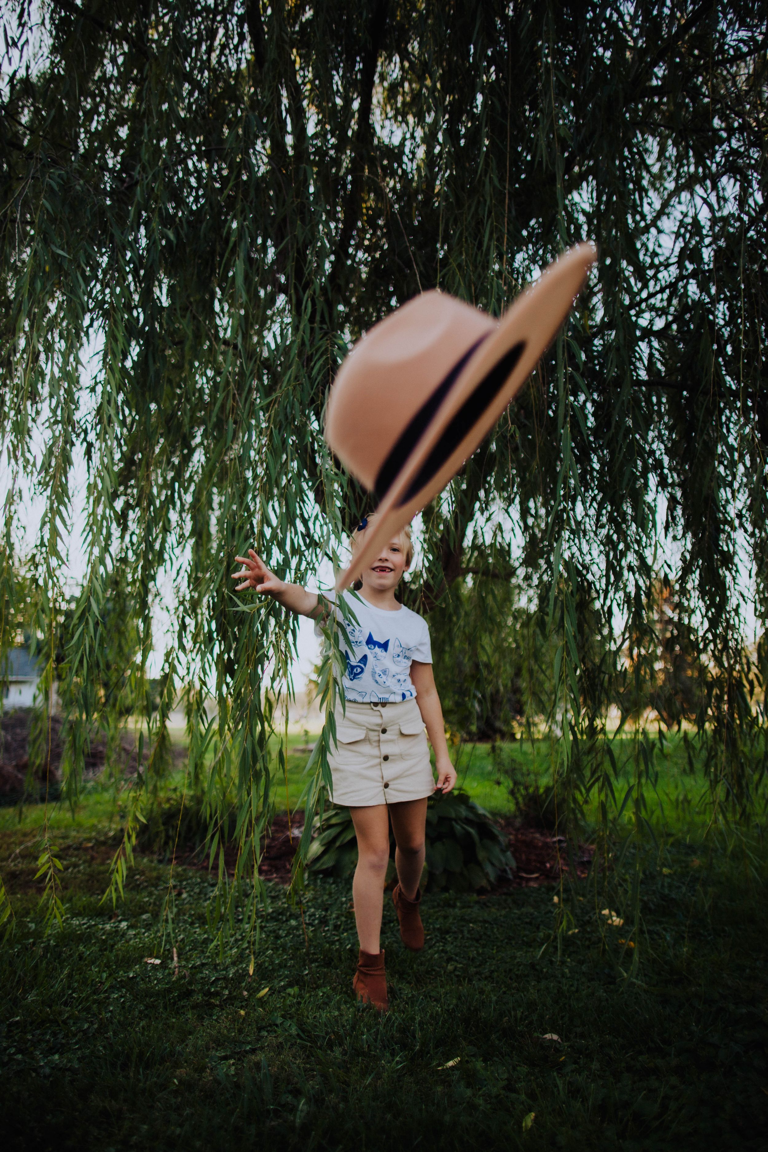 Children playing under drooping willow tree branches in a verdant garden setting.
