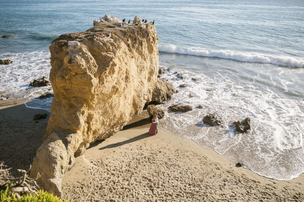 Rocky coastal formation with crashing waves against a beach cliff during sunset.
