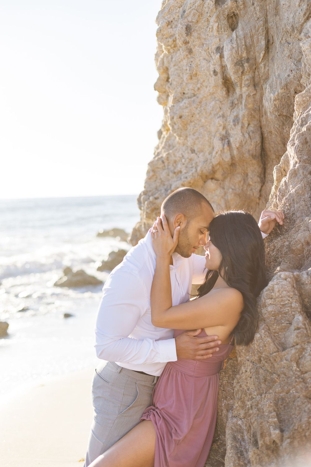 Intimate couple moment against rocky beach cliff during sunset.