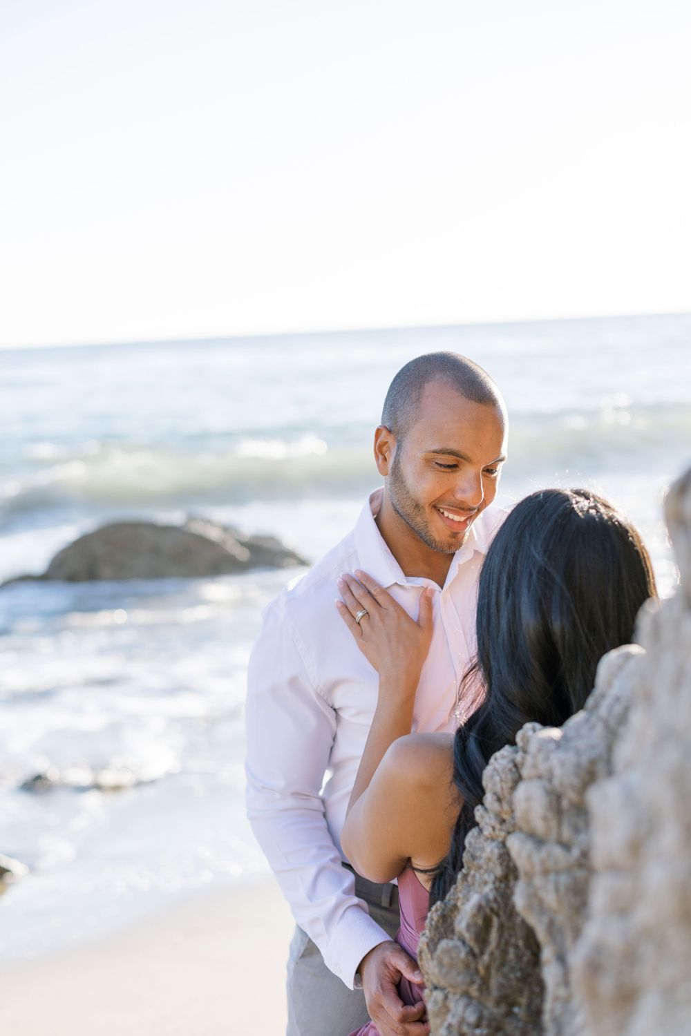 A joyful couple shares a tender moment against a sunny coastal backdrop.