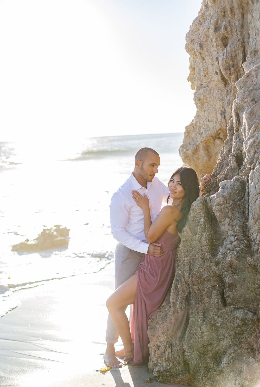 Romantic beach photoshoot with couple posed against coastal cliffs.