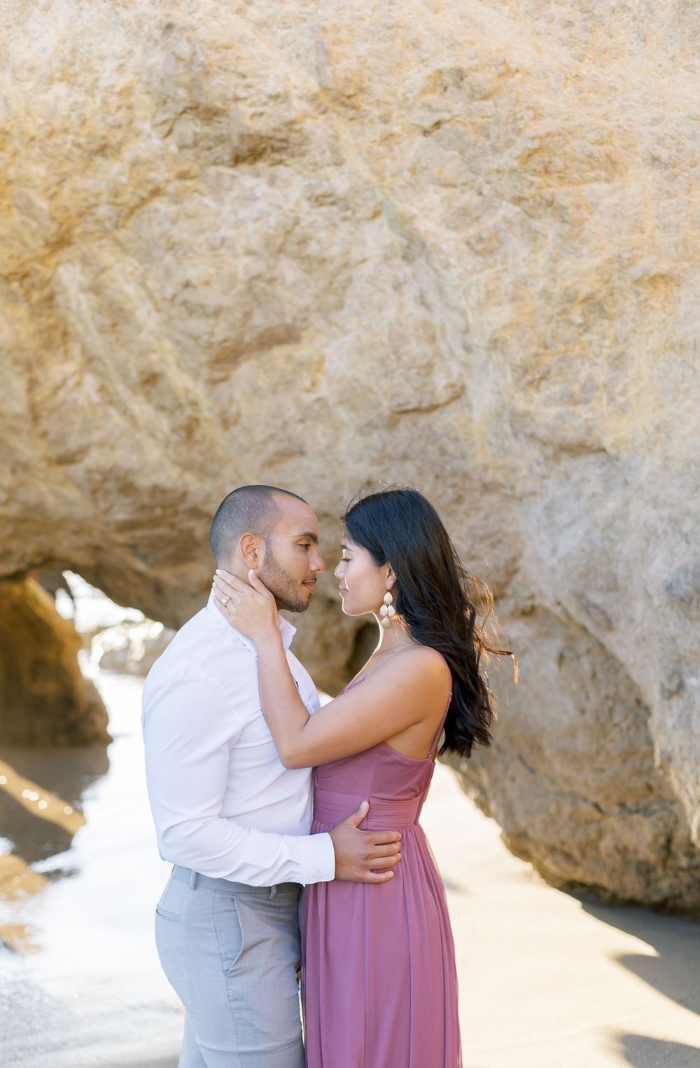 A romantic beach portrait of a couple in an intimate embrace near coastal rock formations.