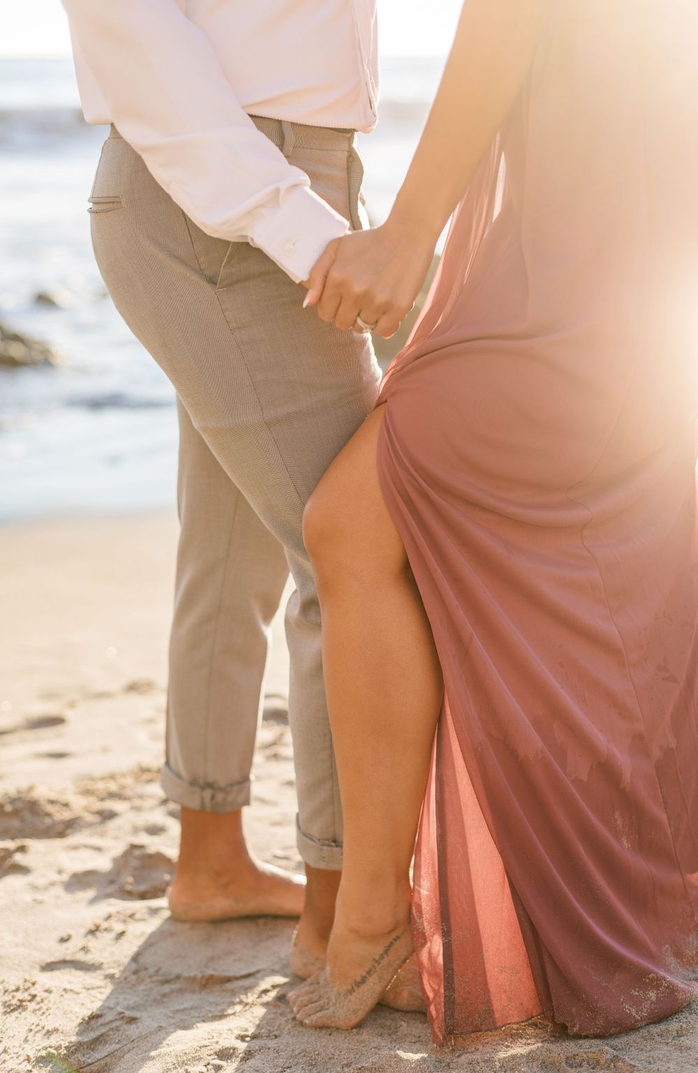 Close-up of feet and flowing dress fabric on sandy beach during romantic photoshoot.