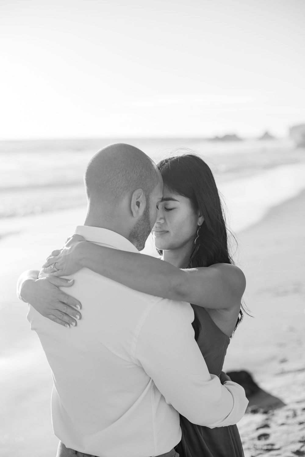 Black and white photo of couple embracing on beach with soft lighting.