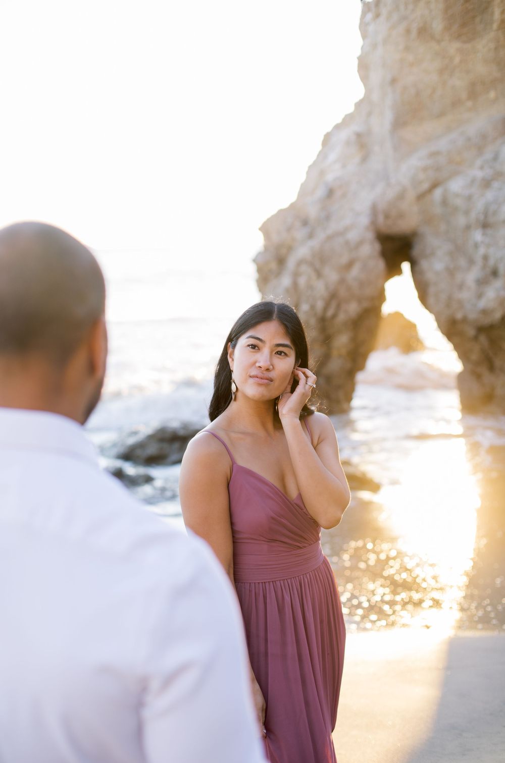 A woman in a mauve dress poses at sunset with natural rock formations in the background.