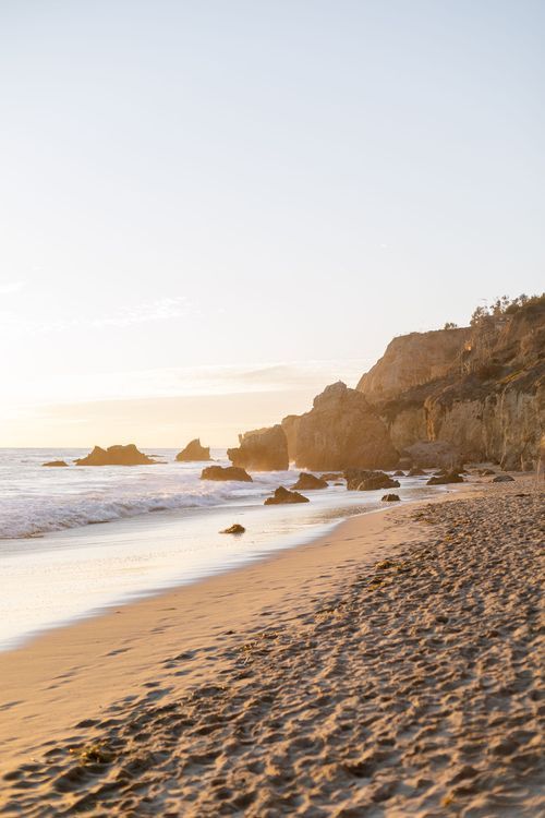 A serene beach landscape with golden cliffs and crashing waves during sunset in California.