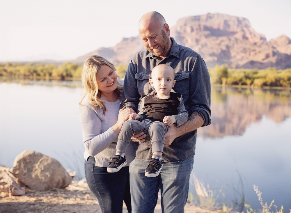 Family photo session at sunset by a scenic lake with mountains in the background.