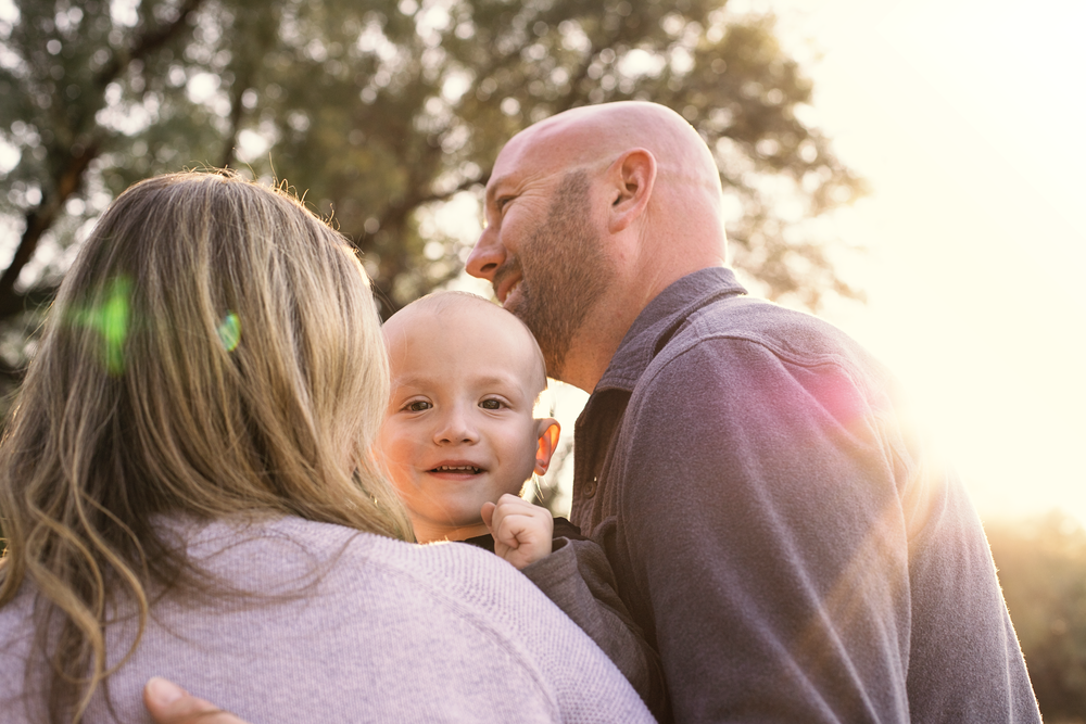Family embraces during golden hour photography session with natural backlighting.
