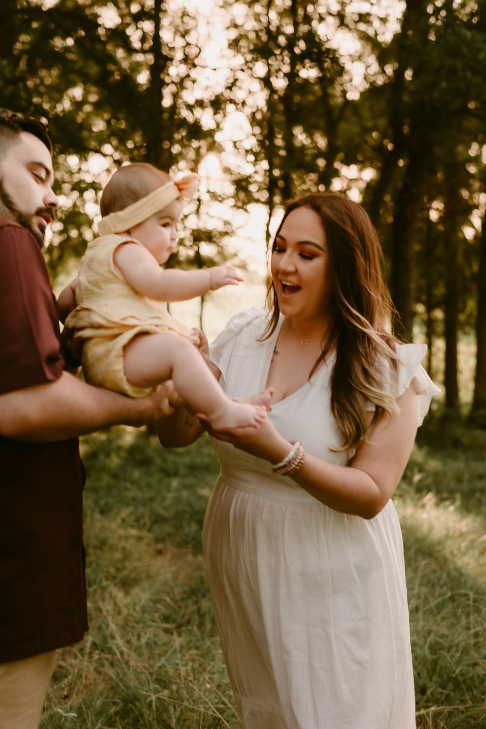 A loving family moment captured in golden hour lighting as they pass their baby between them.