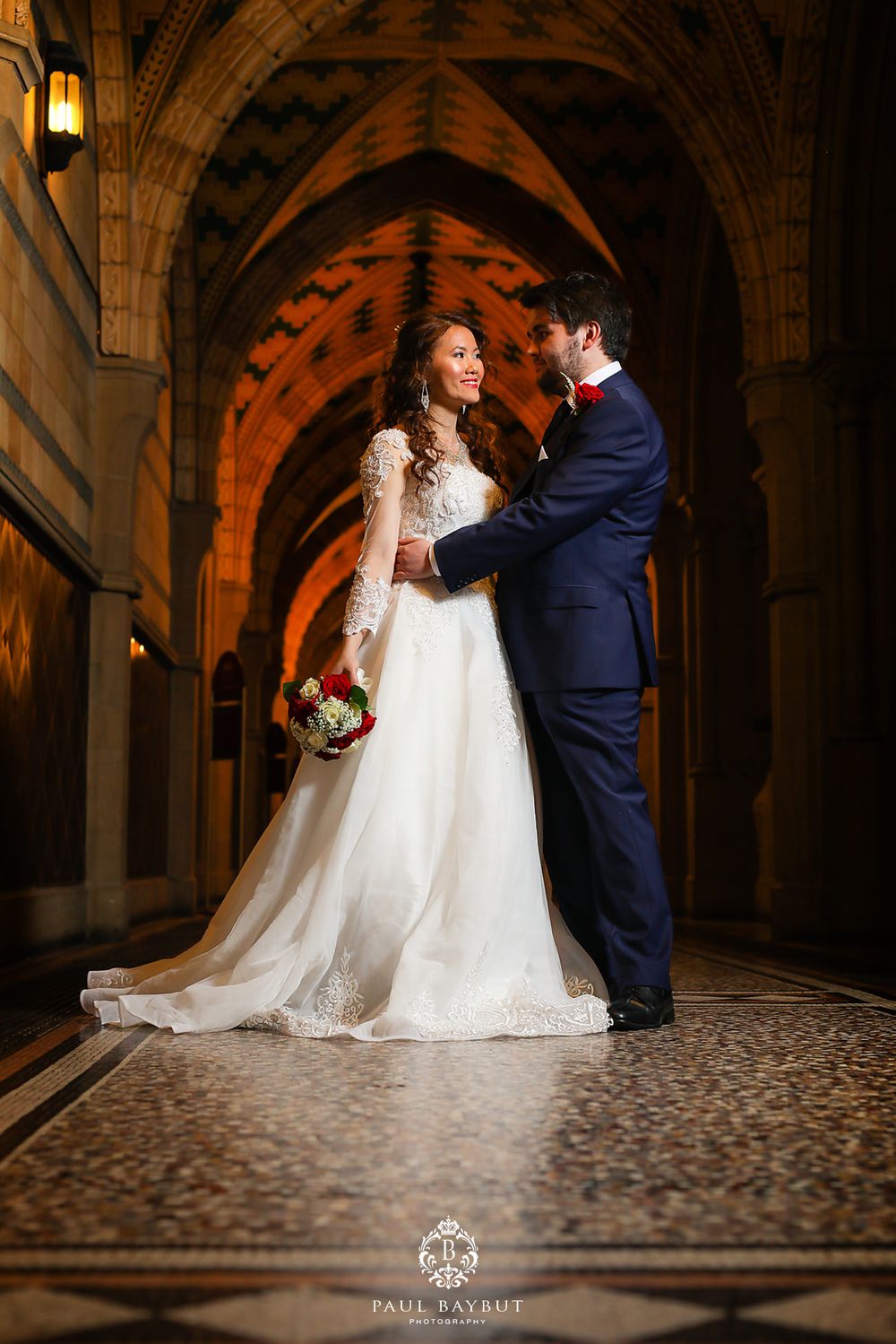 A wedding couple poses in a gothic archway with dramatic lighting and architectural details.