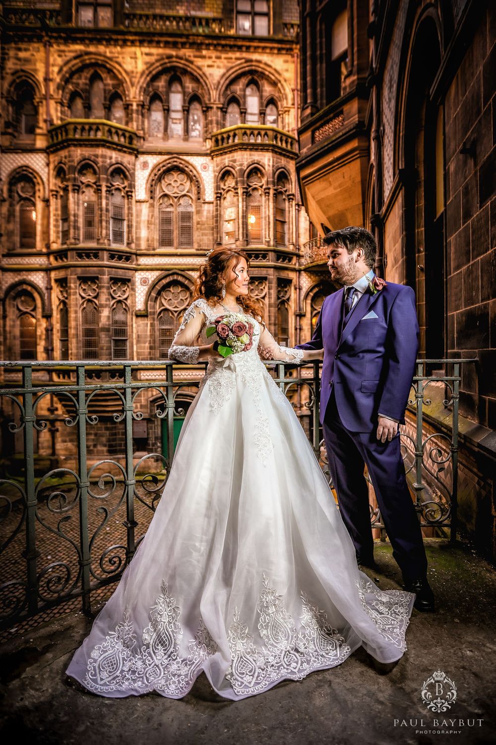 Wedding couple poses against ornate gothic architecture and ironwork.