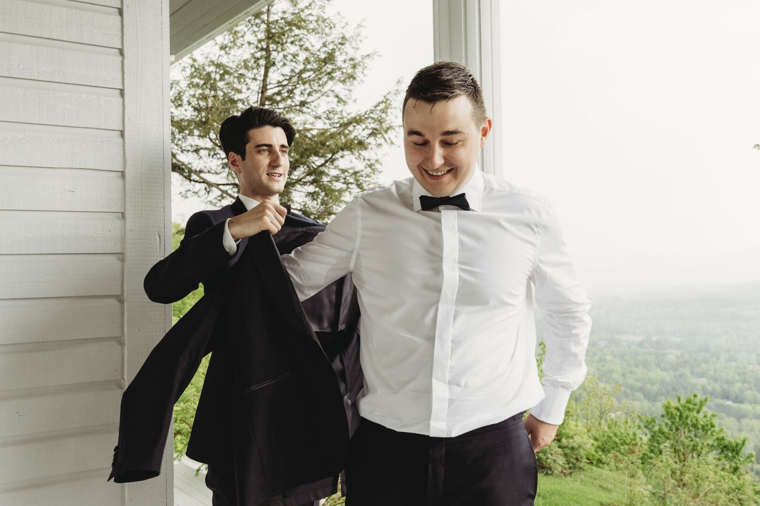 Two people in formal attire preparing their outfits on a white porch.