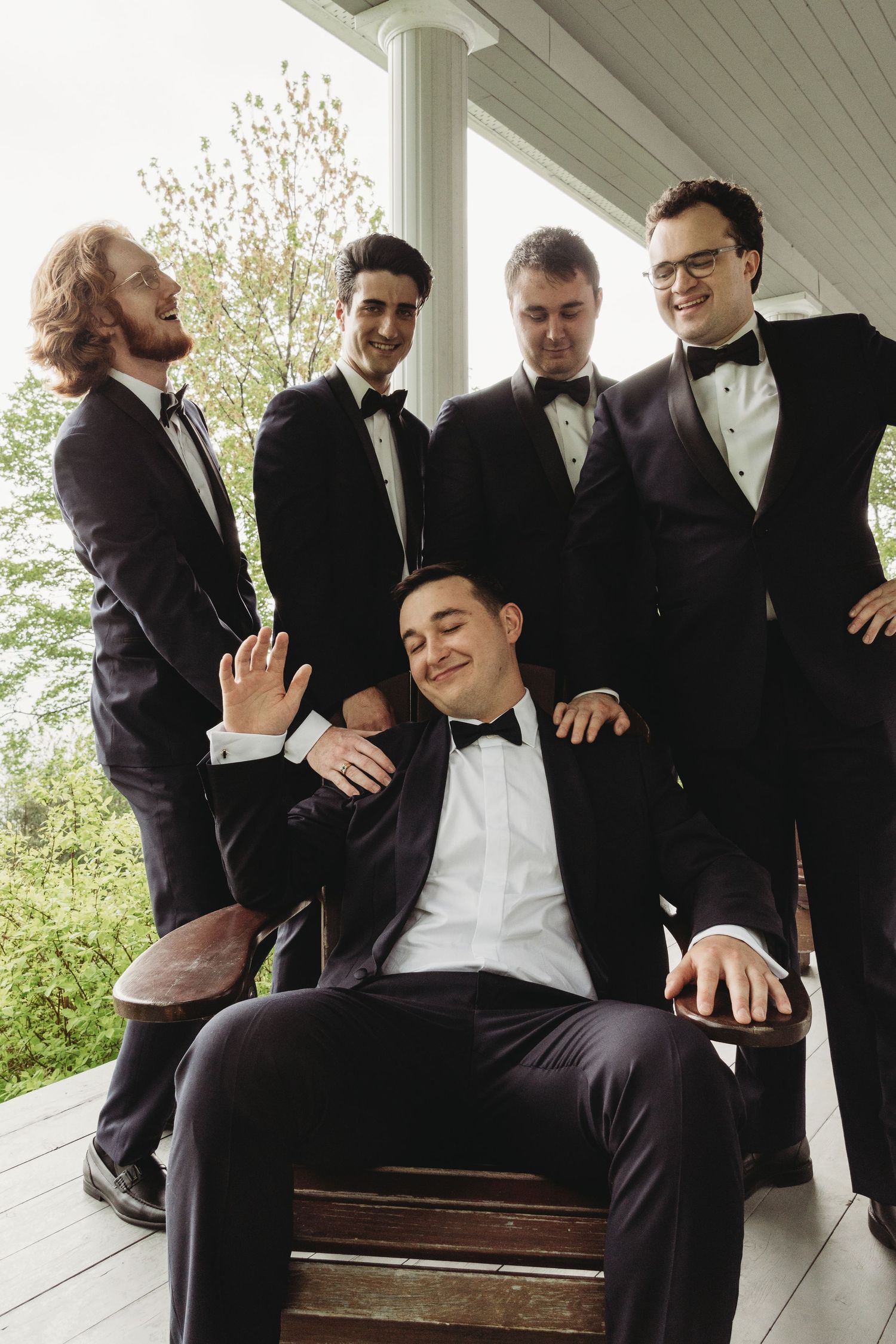 Group in formal attire posing together on a white porch with one seated in the center.