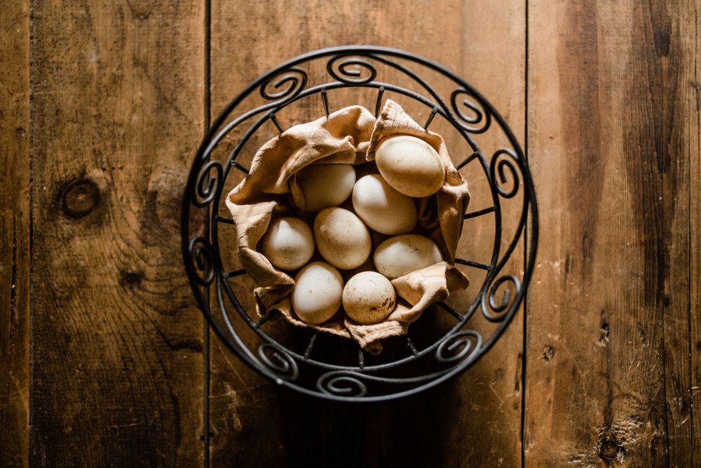 Artistic display of fresh eggs in decorative wire baskets on wooden surface.