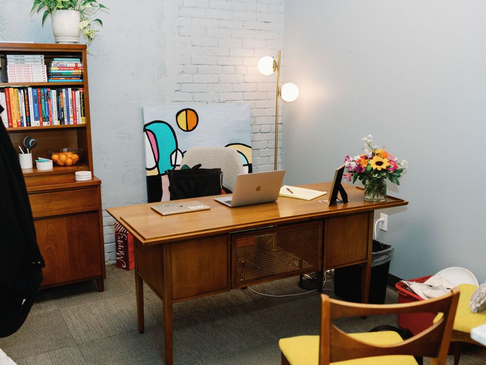 Mid-century modern office space with wooden desk, white brick walls, and bookshelves.