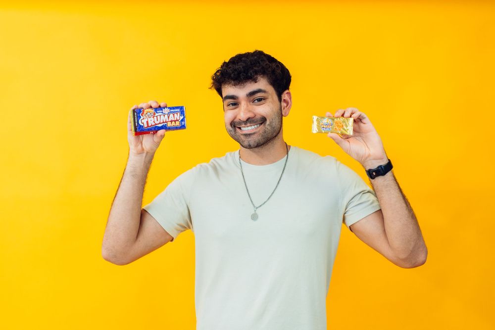 Person holding a candy bar against vibrant yellow background.
