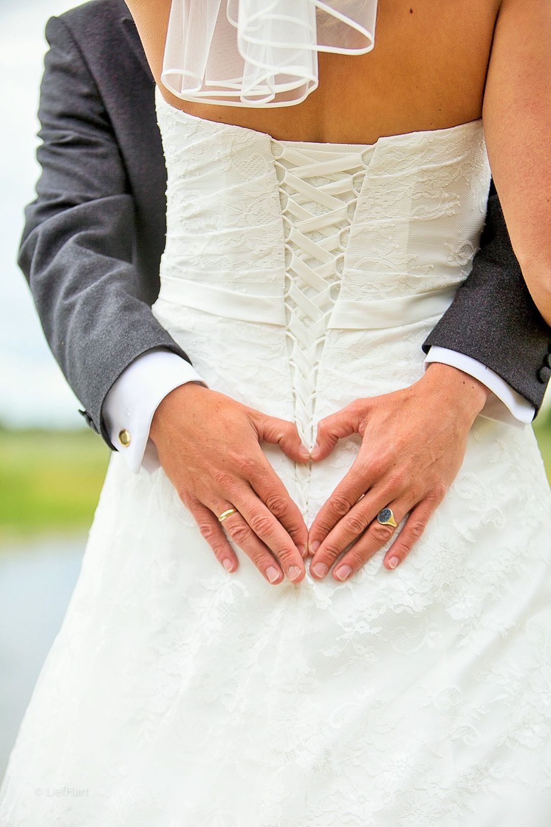 Close-up detail of corset back wedding dress with groom's hands forming heart shape.