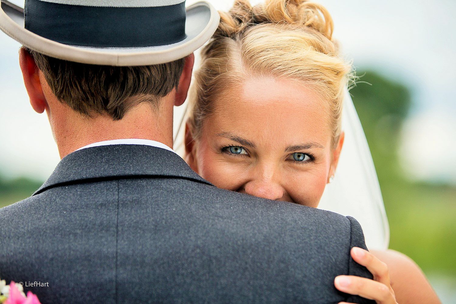 A romantic wedding embrace with the groom in a grey suit and porkpie hat.