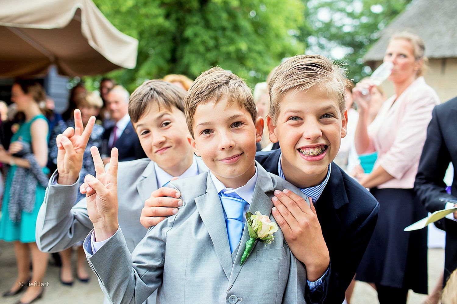 Young groomsmen in light blue ties and grey suits making peace signs.