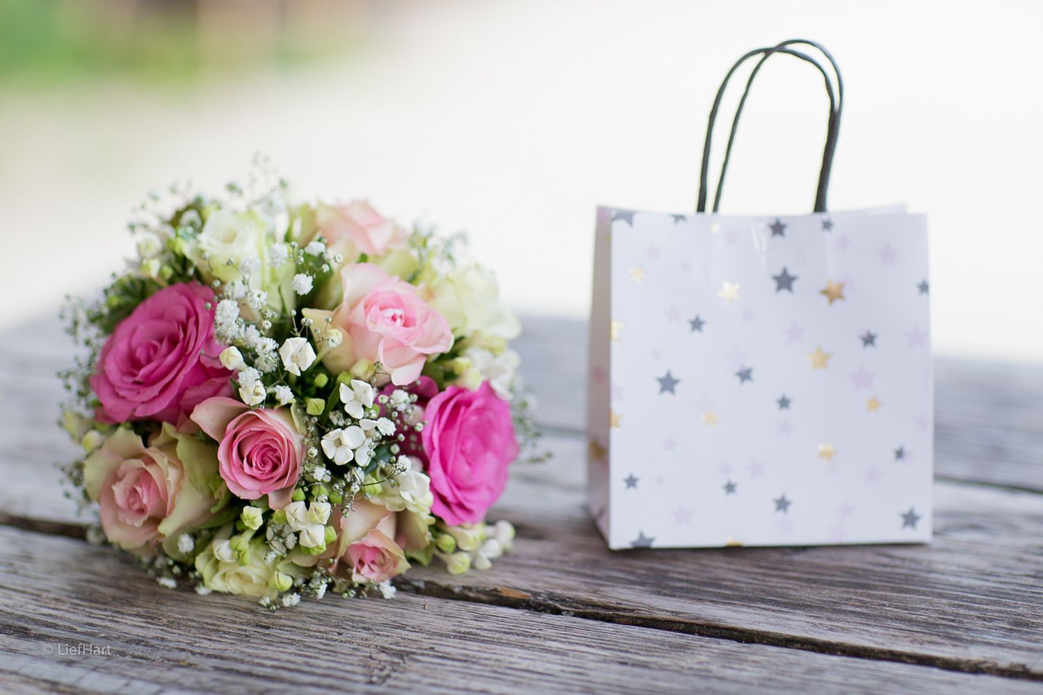 Wedding bouquet with pink roses and white flowers next to a polka dot gift bag.