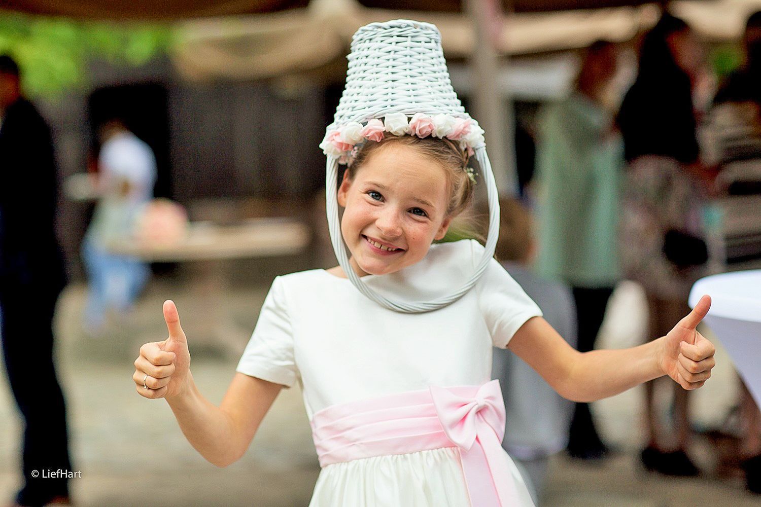 Young attendant wearing a white dress and decorative headpiece giving thumbs up.