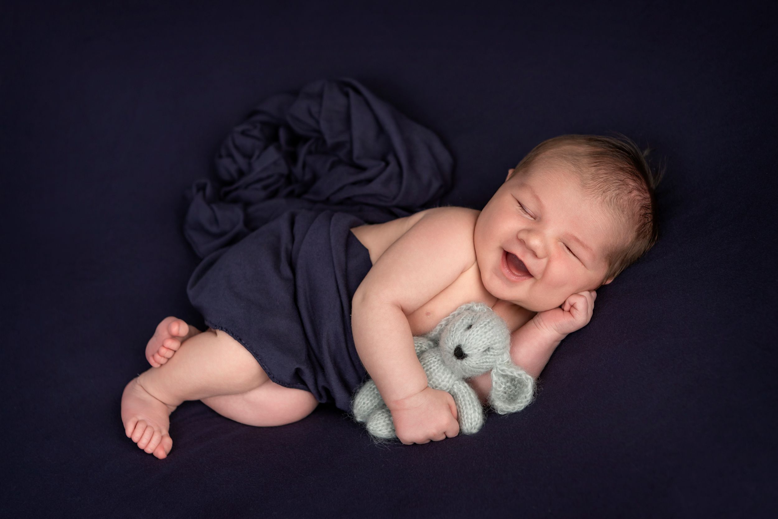 Sleeping baby boy wrapped in dark navy blue with a big smile