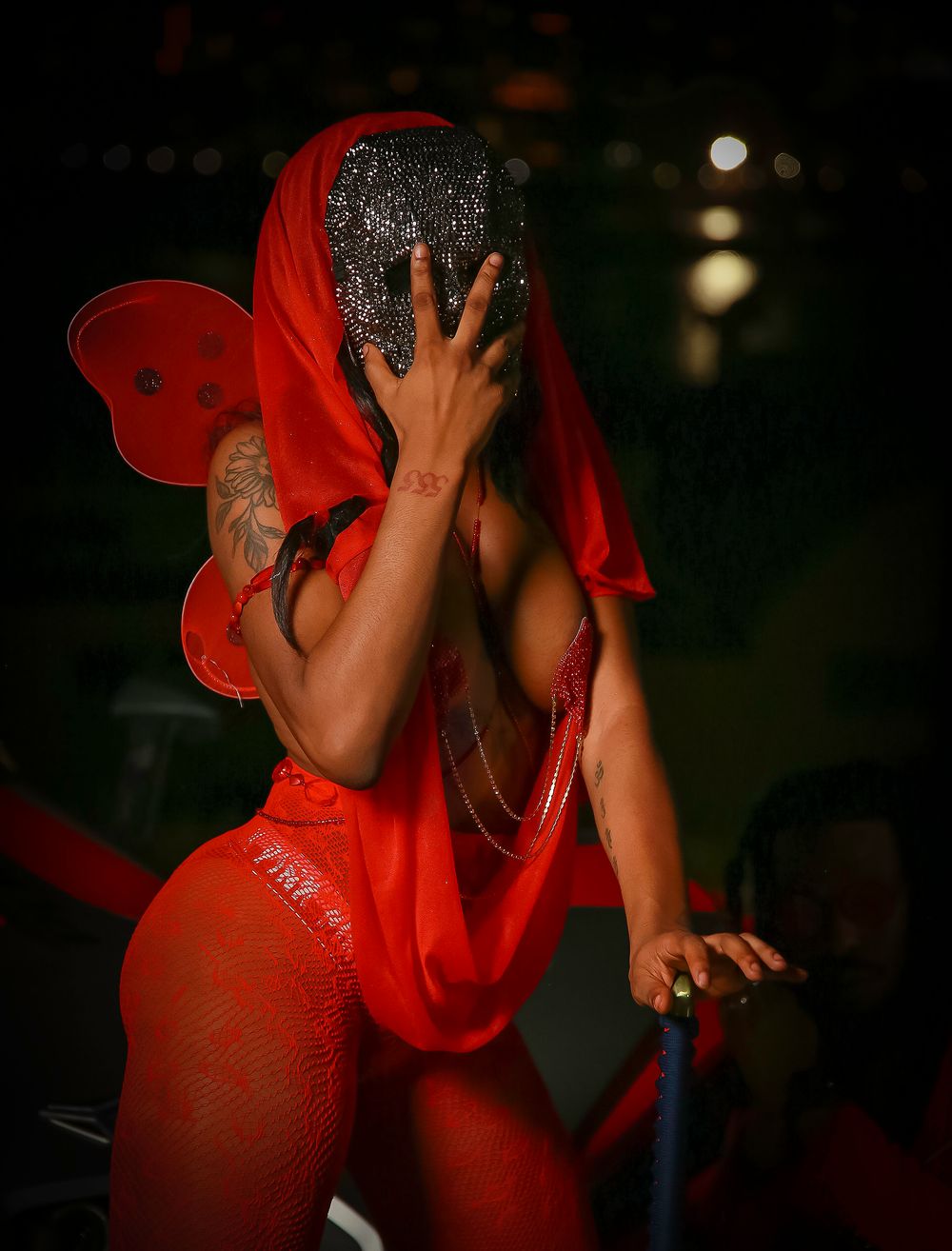 Performer in bright red costume with sheer fabric and butterfly wings dancing on stage in dramatic lighting.
