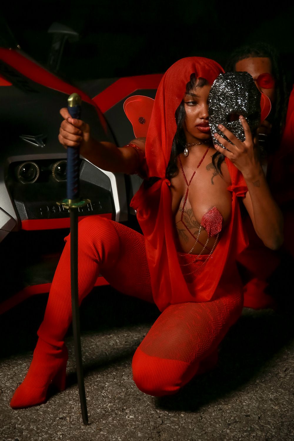 Person in vibrant red outfit striking a dramatic pose against dark background while holding a reflective object.