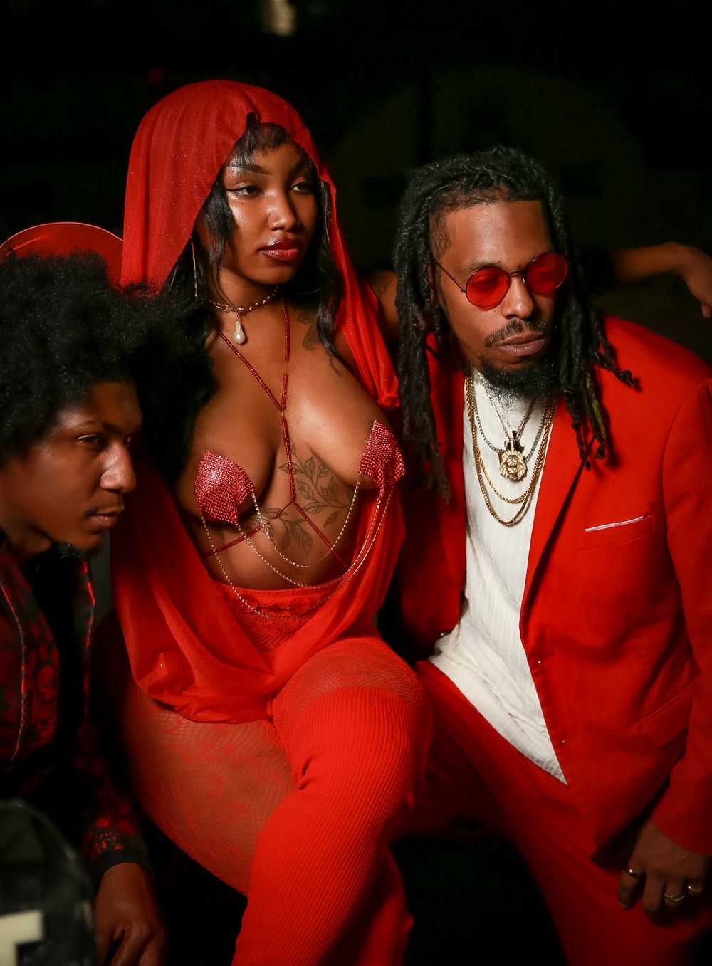 Three people in red attire pose together during a stylized photoshoot.