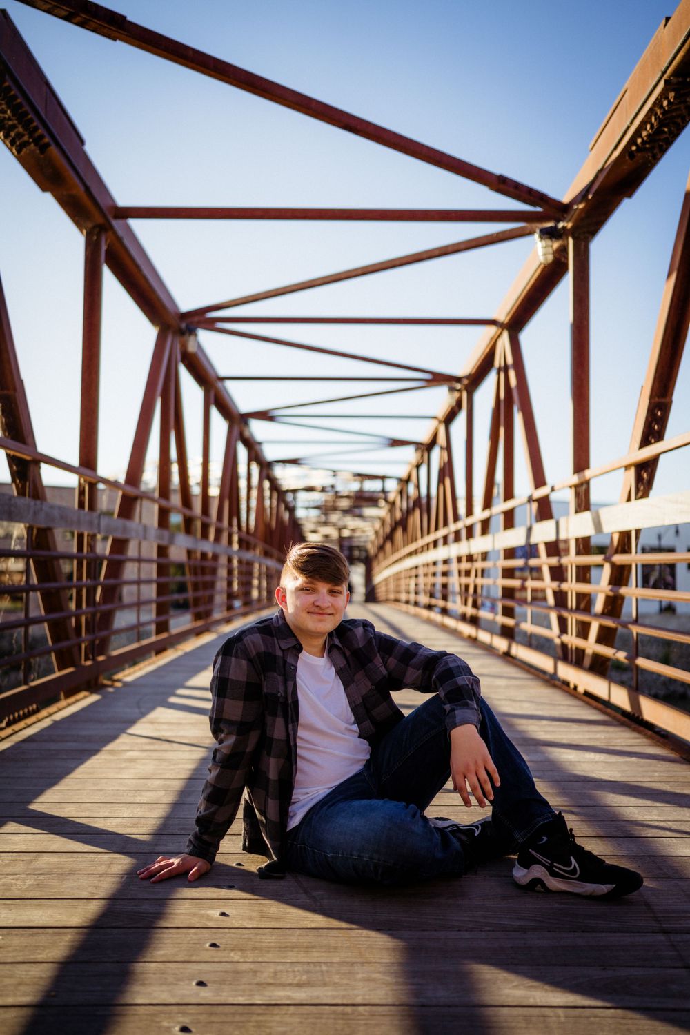 Person relaxes on wooden planks of bridge with geometric metal framework overhead.