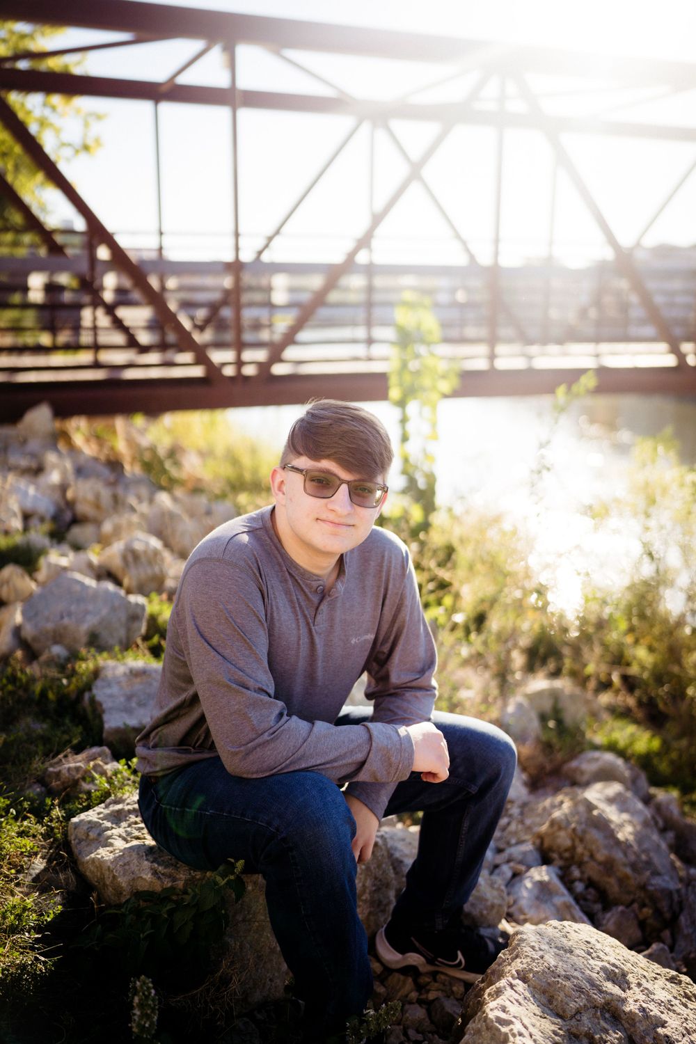 Portrait of person sitting on rocks by metal bridge during golden hour sunset.